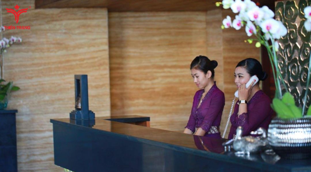 Nữ lễ tân spa chuyên nghiệp đang tươi cười đón tiếp khách hàng tại quầy lễ tân sang trọng, thể hiện sự tận tâm trong công việc lễ tân spa cần làm những gì