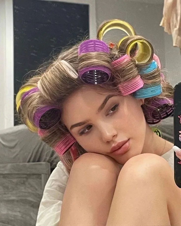 Hình ảnh cận cảnh một người đang thoa kem dưỡng hoặc dầu bóng cho tóc uốn xoăn lơi, thể hiện bước dưỡng tóc