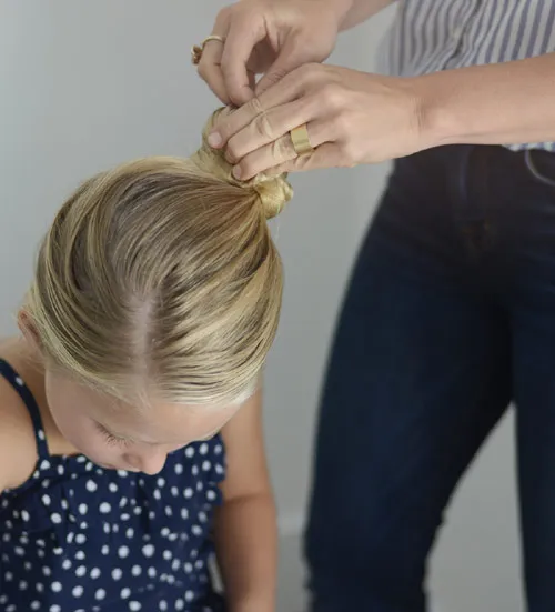 Thực hiện thao tác buộc và xoắn tóc sang một bên để chuẩn bị búi tròn, bước cơ bản trong cách búi tóc cute