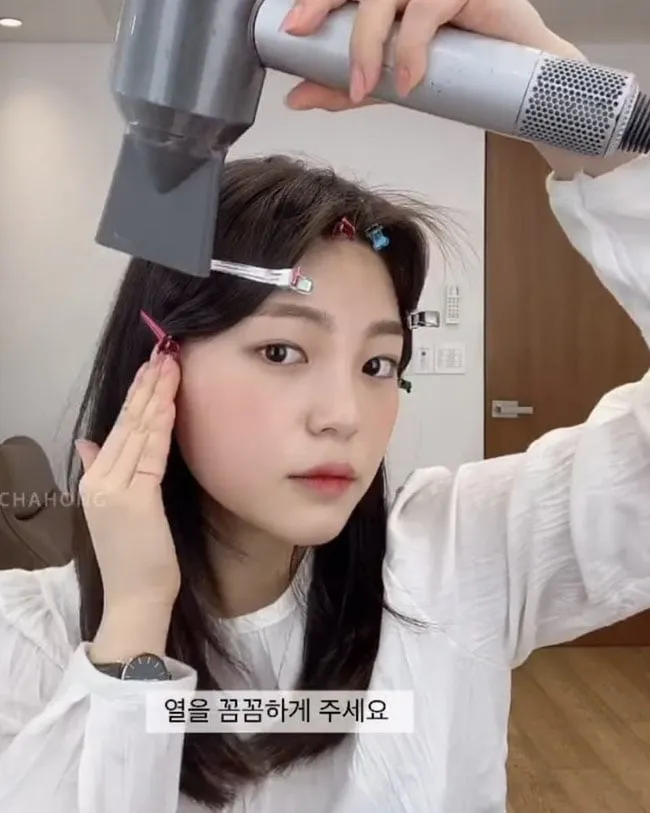 Cô gái đang sử dụng máy sấy tóc ở chế độ nhiệt thấp để làm khô và định hình tóc đã được kẹp