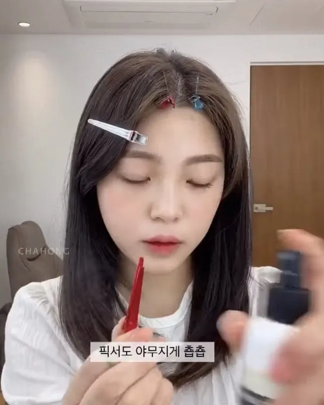 Cô gái đang sử dụng kẹp tóc để cố định phần chân tóc ở hai bên đường ngôi giữa