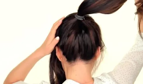 Cô gái đang thực hiện bước cột tóc đuôi ngựa cao trên đỉnh đầu để tạo nền cho kiểu tóc búi Hàn Quốc