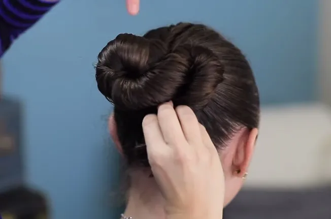 Hình ảnh người hướng dẫn đang xoắn và cuộn lọn tóc còn lại để tạo hình vòng cung thứ hai, hoàn thành hình số Tám nằm ngang