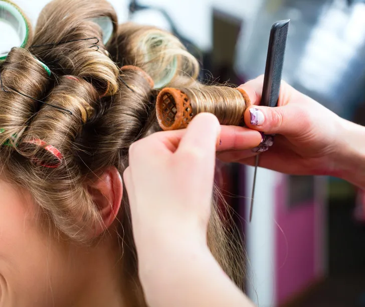 Một phụ nữ đang dùng serum dưỡng tóc để cố định và tăng độ bóng cho mái tóc xoăn vừa được tháo lô cuốn