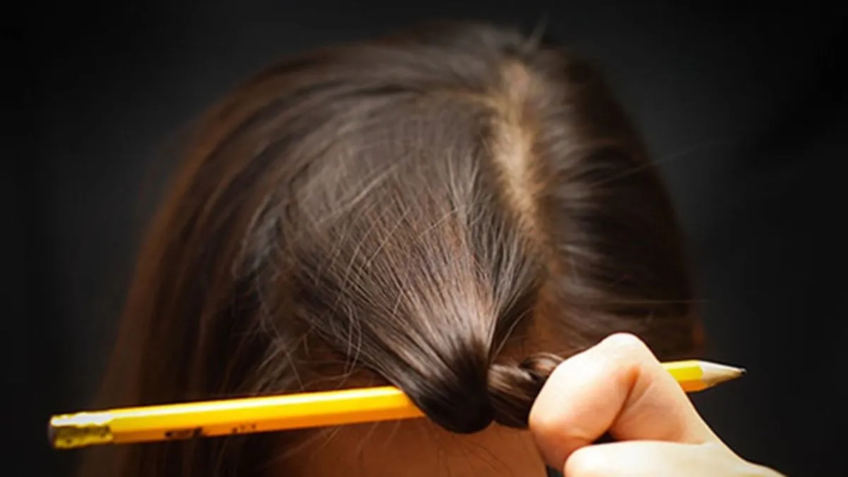 Một cây bút chì được dùng để quấn lọn tóc nhỏ, minh họa cách uốn tóc tại nhà bằng dụng cụ văn phòng.