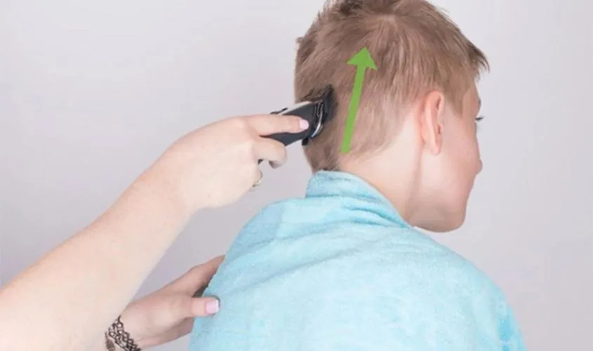 Cắt tóc ở vị trí gáy trước bằng tông đơ cho bé trai theo hướng từ dưới lên
