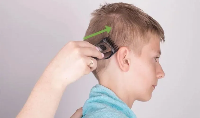 Cắt tóc hai bên đầu bé trai bằng tông đơ, di chuyển từ gáy đến mang tai