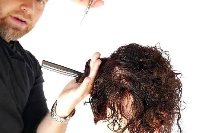 Người thợ đang kẹp lọn tóc nhỏ giữa hai ngón tay và cắt tỉa theo chiều dọc để tạo lớp layer