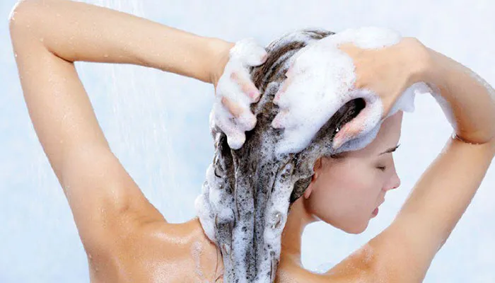 Người phụ nữ đang gội đầu bằng nước mát và hạn chế dùng dầu gội sau khi tẩy tóc