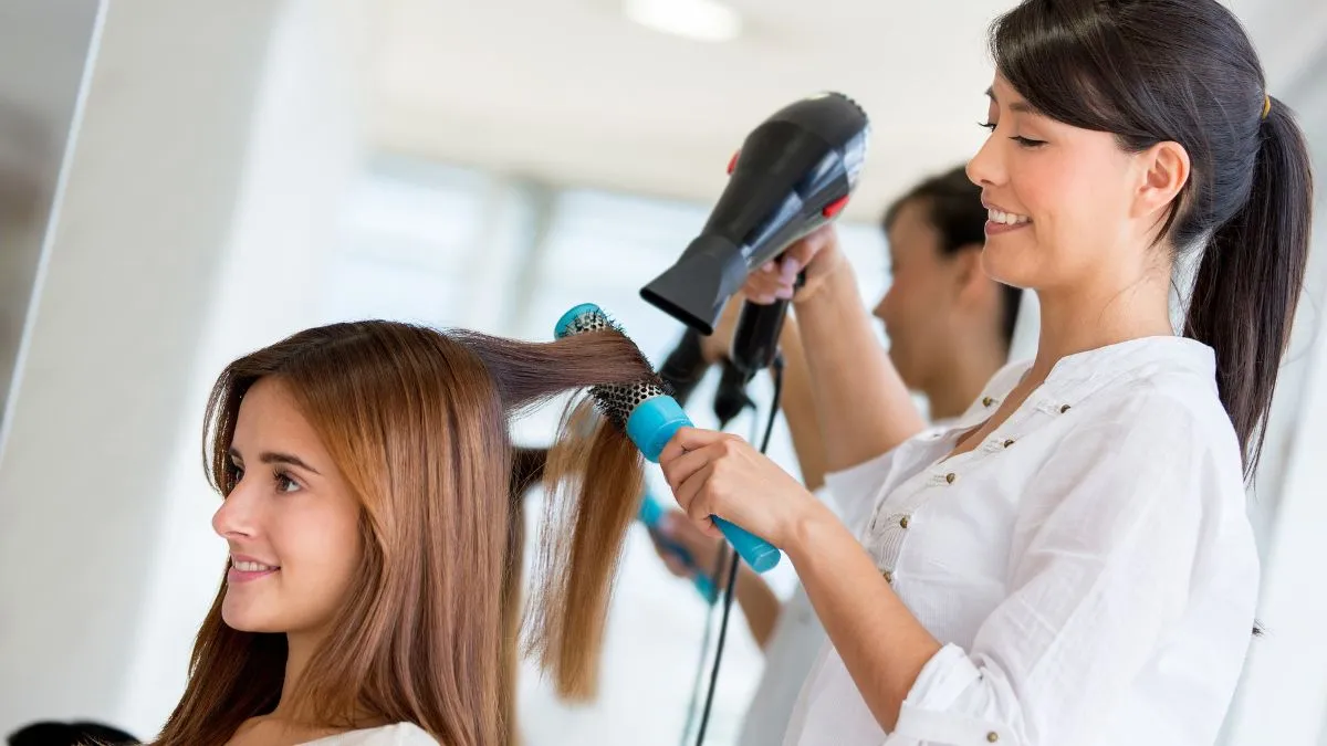 Hình ảnh một người phụ nữ đang sấy tóc bằng máy sấy cầm tay, thể hiện thao tác sấy tóc đúng cách để giữ độ phồng