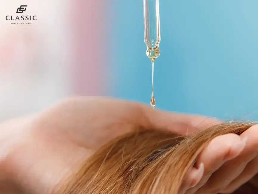 Bàn tay chuyên gia đang trộn tinh dầu Moroccanoil với kem ủ hoặc kem tạo kiểu trên một chiếc bát nhỏ