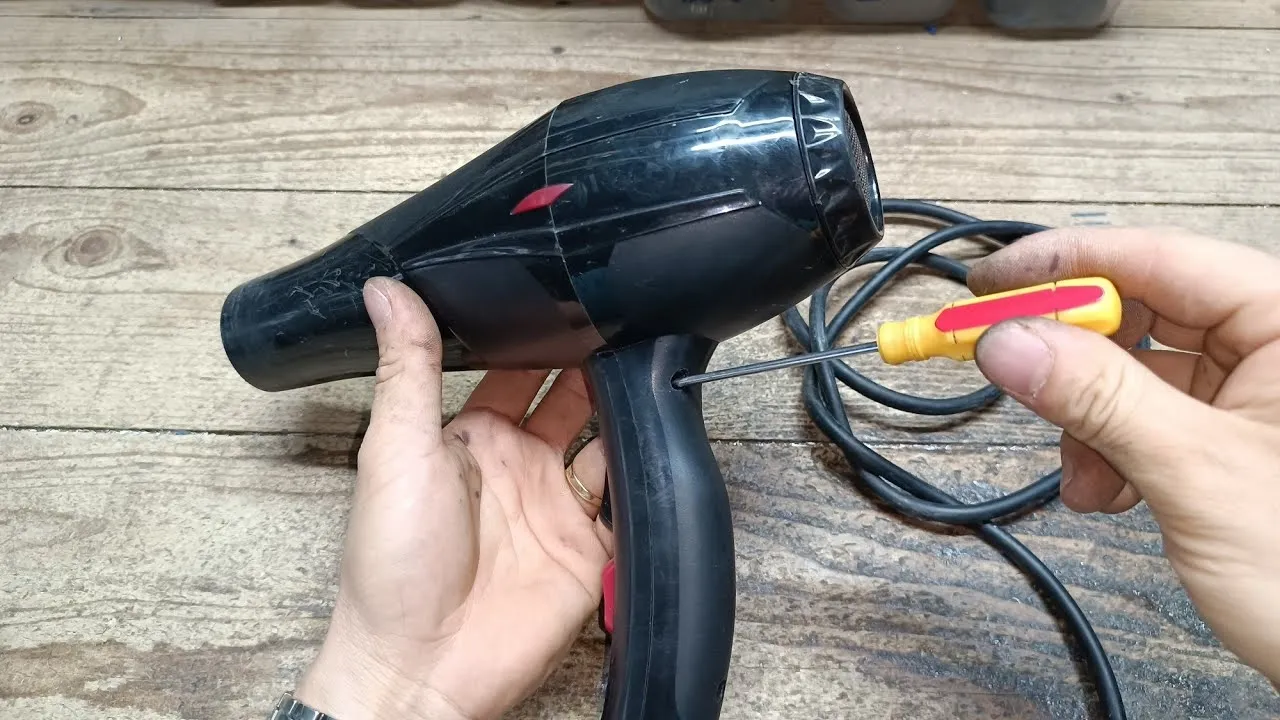 Sử dụng tua vít để xác định và tháo ốc vít cố định trên tay cầm máy sấy tóc