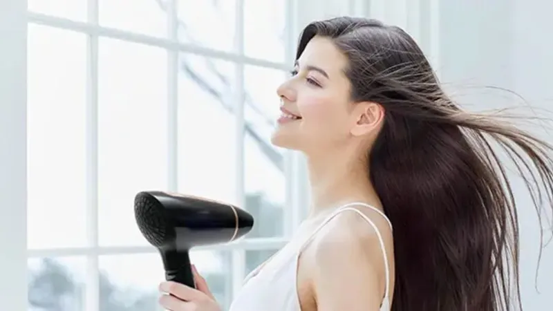 Bàn tay đang điều chỉnh chế độ nhiệt và luồng gió trên thân máy sấy tóc