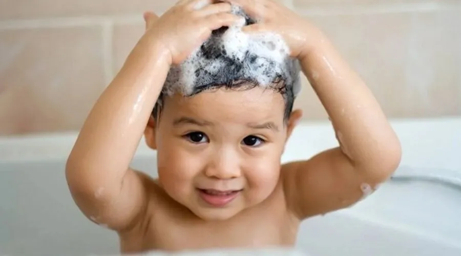 Mẹ đang chải tóc nhẹ nhàng cho bé gái 1 tuổi bằng lược mềm, tư thế chăm sóc tóc đúng cách.