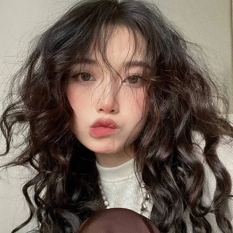 Người phụ nữ đang vuốt nhẹ các lọn tóc xoăn đã được uốn tạo kiểu, thể hiện độ mềm mượt và không bị khô xơ