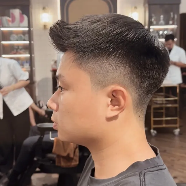 Một người đàn ông đang được thợ cắt tóc sử dụng tông đơ cạo gọn gàng phần tóc xung quanh