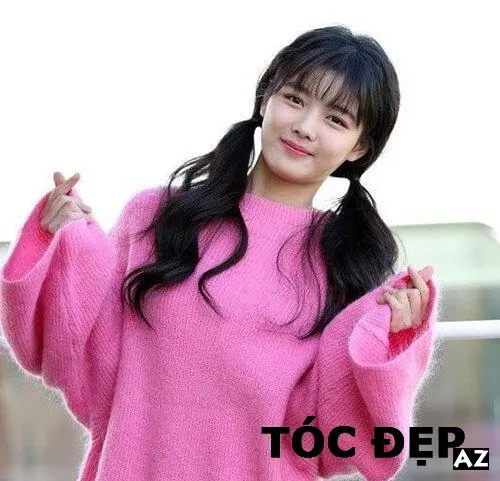 Cô gái với kiểu tóc buộc hai bên thấp, mái tóc hơi xoăn nhẹ và rủ xuống vai, toát lên vẻ duyên dáng