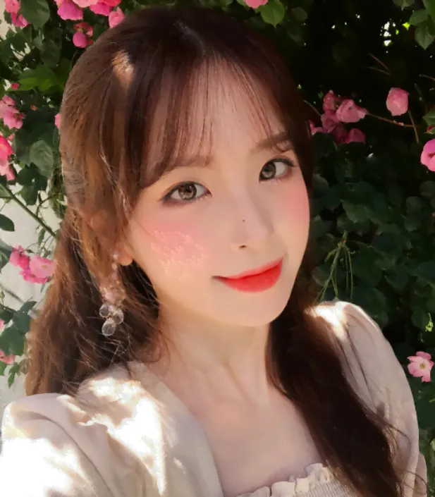 Một phụ nữ với kiểu tóc uốn lơi nhẹ nhàng, trang điểm tông màu đồng và son đỏ, phù hợp cho tiệc văn phòng