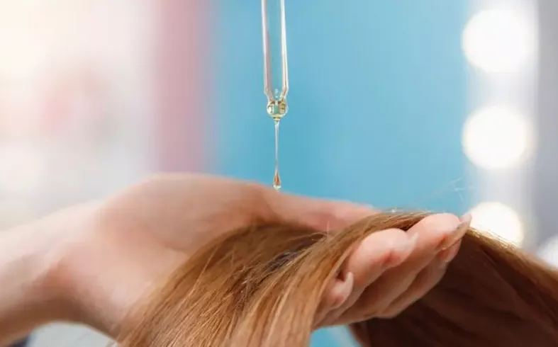 Một phụ nữ đang thoa serum dưỡng tóc lên phần ngọn tóc để tăng độ bóng và giảm xơ rối