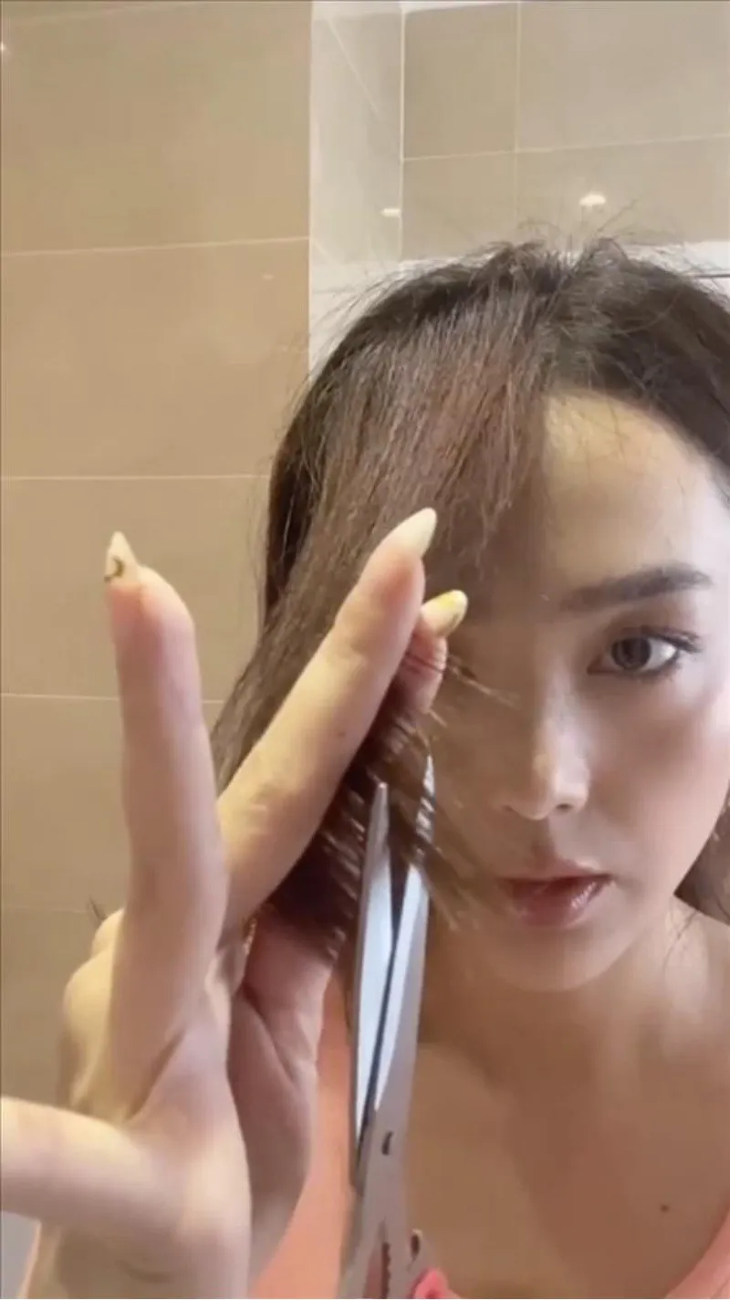 Tỉa tóc mái bay cần chia tóc làm 2 phần và kẹp tóc bằng ngón tay trỏ, ngón giữa trước khi cắt chéo.