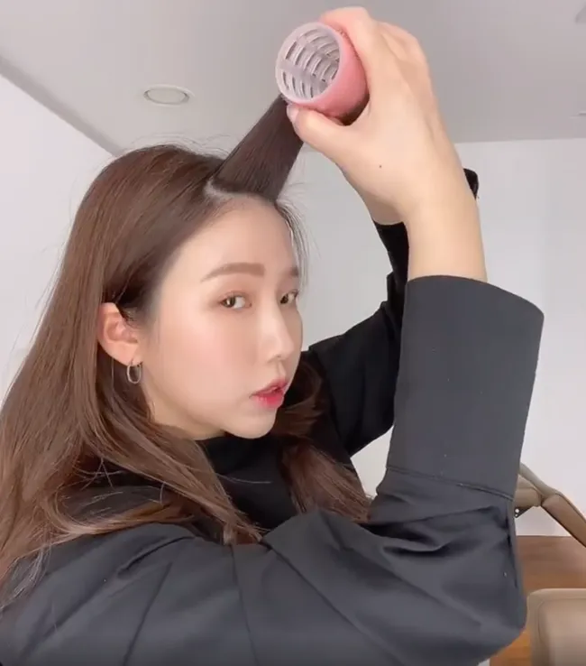 Thao tác sử dụng lô cuốn tóc dính loại lớn để cuốn phần tóc mái hoặc lọn tóc nhằm tạo độ cong và độ phồng bồng bềnh