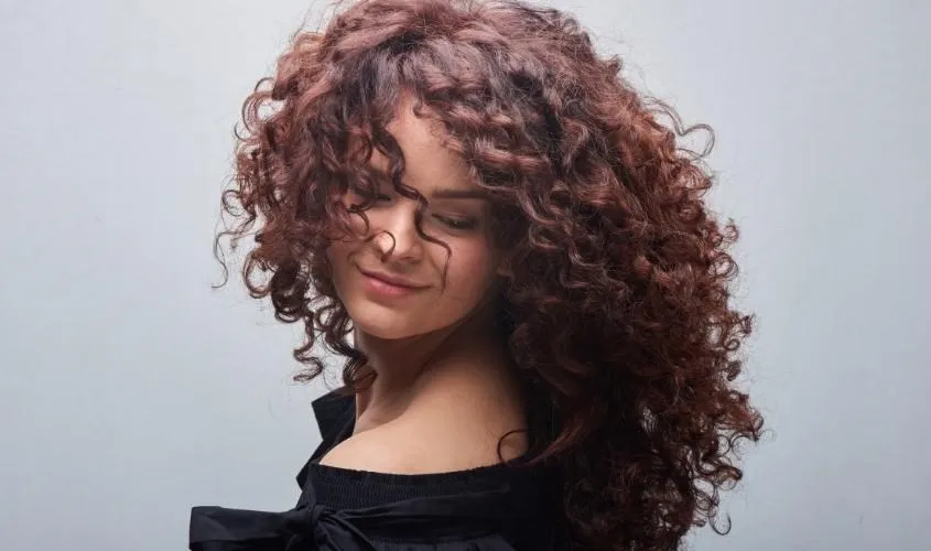 Một cô gái có mái tóc xoăn uốn lọn lớn đang kiểm tra tóc, minh họa quy tắc 72 giờ đầu tiên trong cách để giữ nếp tóc