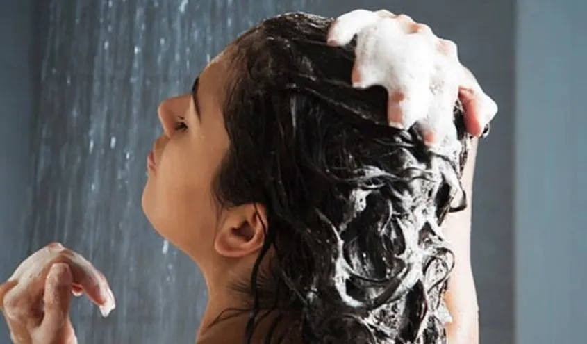 Người phụ nữ đang nhẹ nhàng xả tóc bằng nước lạnh để bảo vệ cấu trúc tóc xoăn